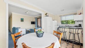 Une cuisine compacte équipée d’un réfrigérateur, d’une cuisinière et de tabourets de bar. Une table à manger avec des chaises se trouve au premier plan.