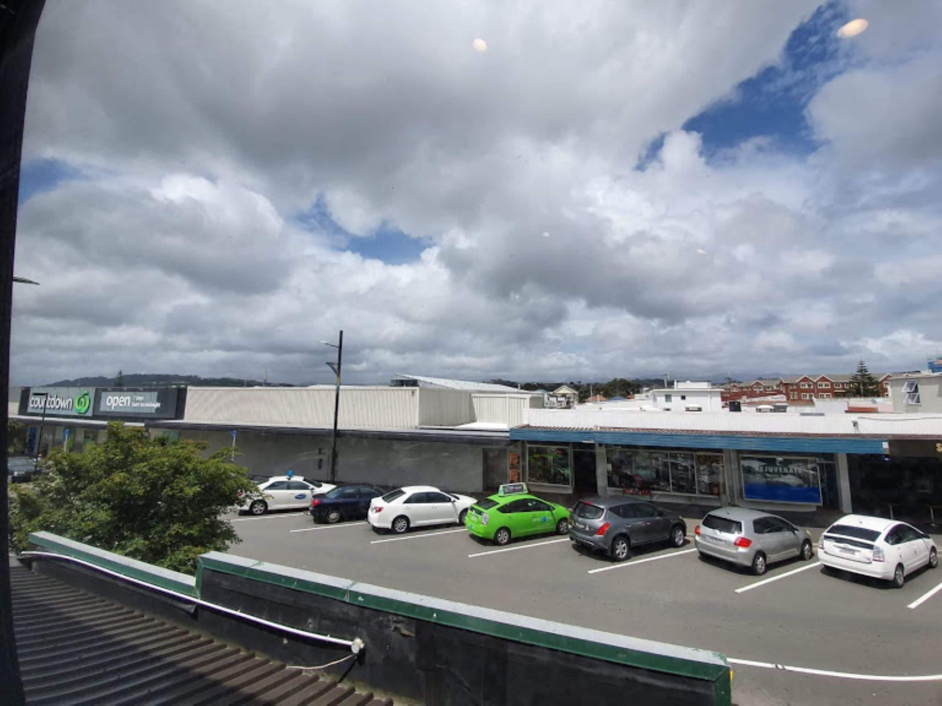 Un estacionamiento con varios autos, un edificio con un letrero y un cielo nublado.