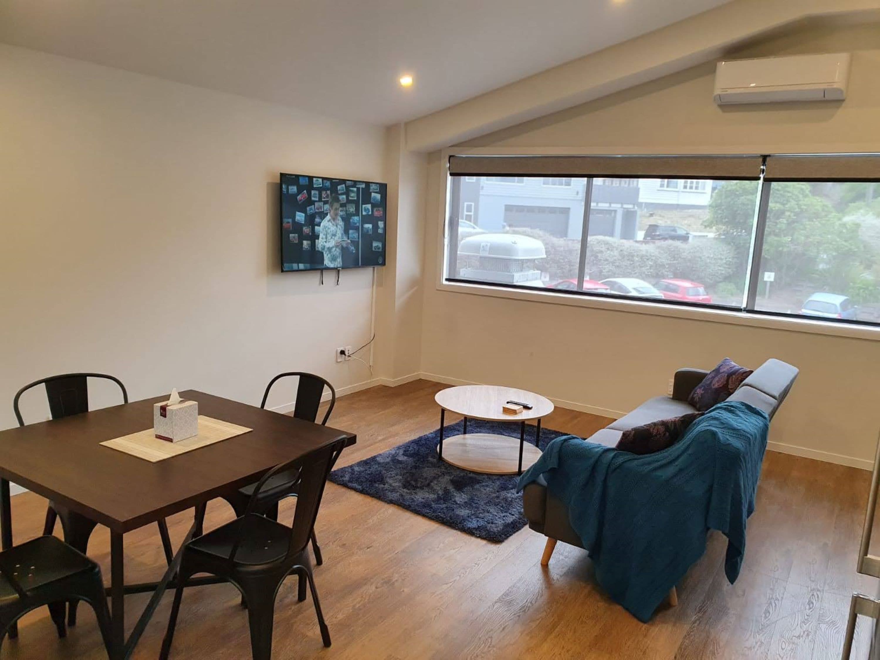 Un moderno salón con una mesa de comedor, sillas, un sofá y un amplio ventanal con vistas al exterior.