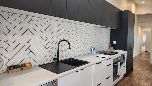 A modern kitchen with a herringbone tile backsplash, a black faucet, and a built-in oven. - U Suites Kilbirnie (Wellington)