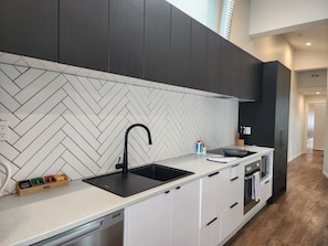 A modern kitchen with a herringbone tile backsplash, a black faucet, and a built-in oven. - U Suites Kilbirnie (Wellington)
