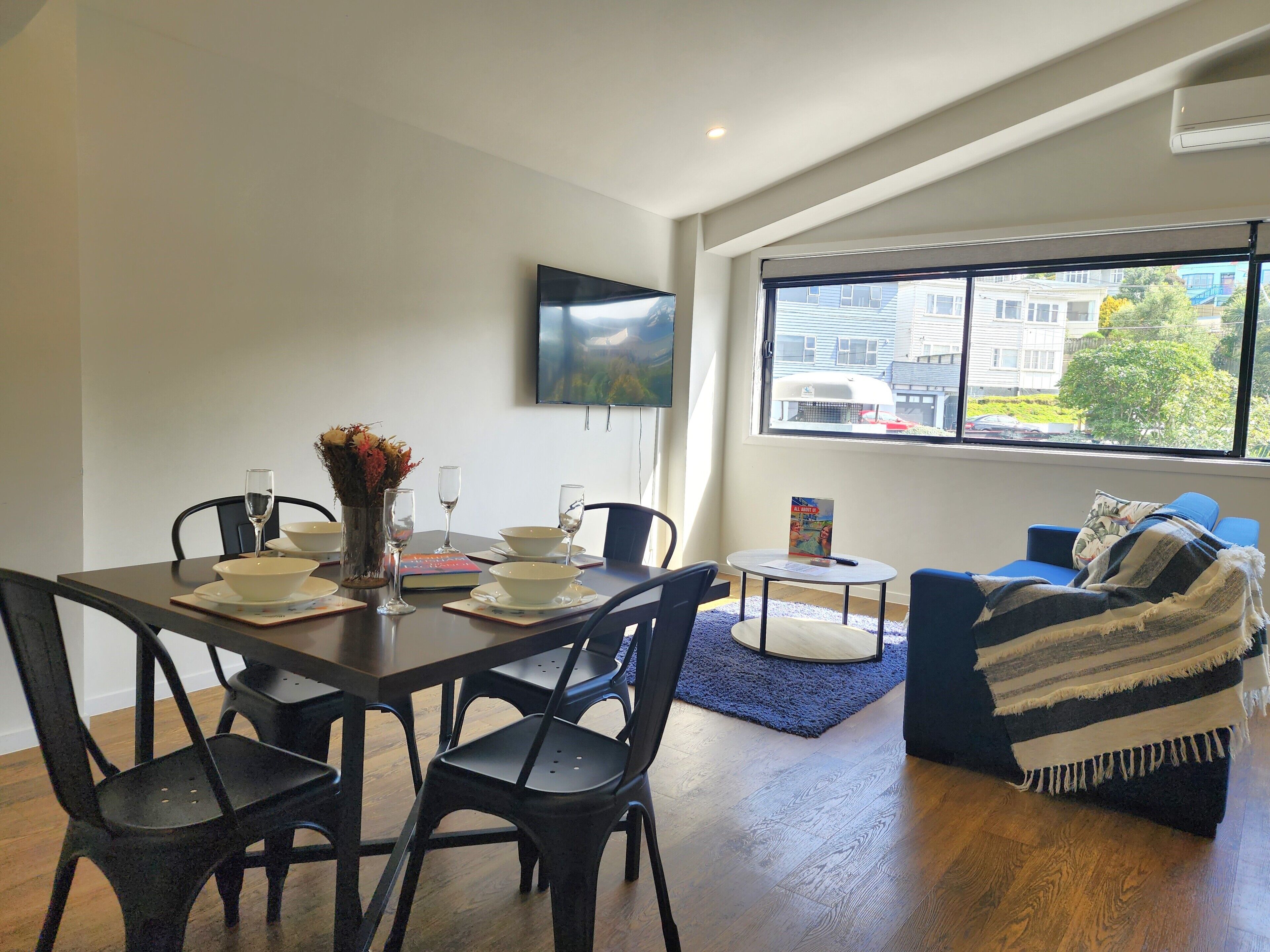 Una sala de estar moderna con comedor, ventanas amplias y un televisor de pantalla plana en la pared.