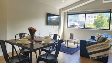 Una sala de estar moderna con comedor, ventanas amplias y un televisor de pantalla plana en la pared.