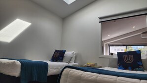 A bedroom with two beds, a skylight, and a window with a view of the outside. - U Suites Kilbirnie (Wellington)