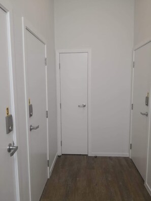 A hallway with white walls and wooden flooring, leading to a closed door with a handle and a lock. - U Suites Kilbirnie (Wellington)