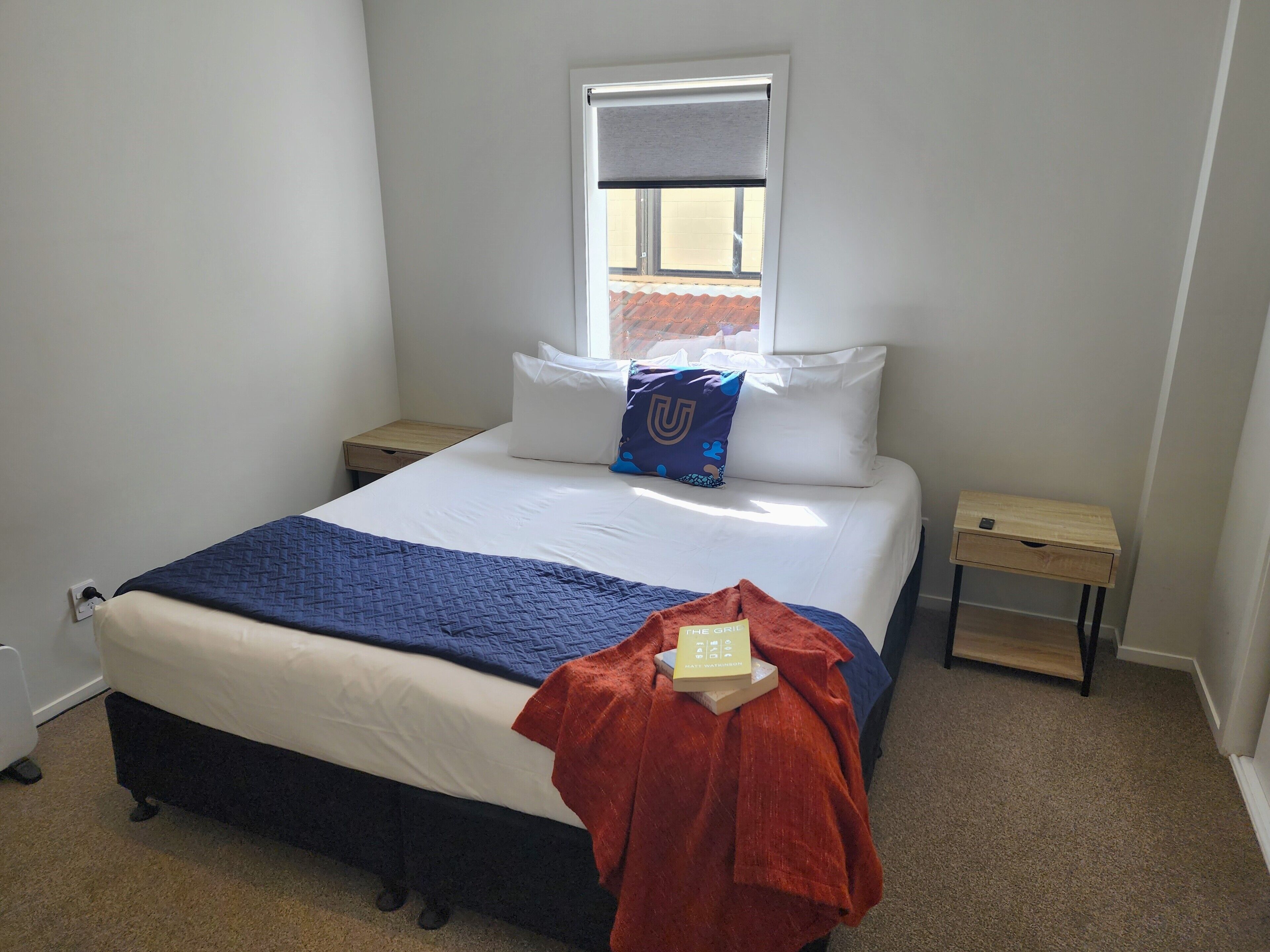 A neatly arranged bedroom with a bed, two bedside tables, a window, and a view of the outside.