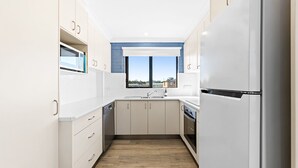 A modern kitchen with white cabinets, a built-in oven, and a stainless steel refrigerator. - Apollo Unit 21 - 1st Floor (Narooma)