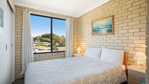Ein Hotelzimmer mit einem großen Bett, einem Fenster mit Vorhängen, einer Ziegelwand, einem Gemälde und einem Nachttisch mit einer Lampe.