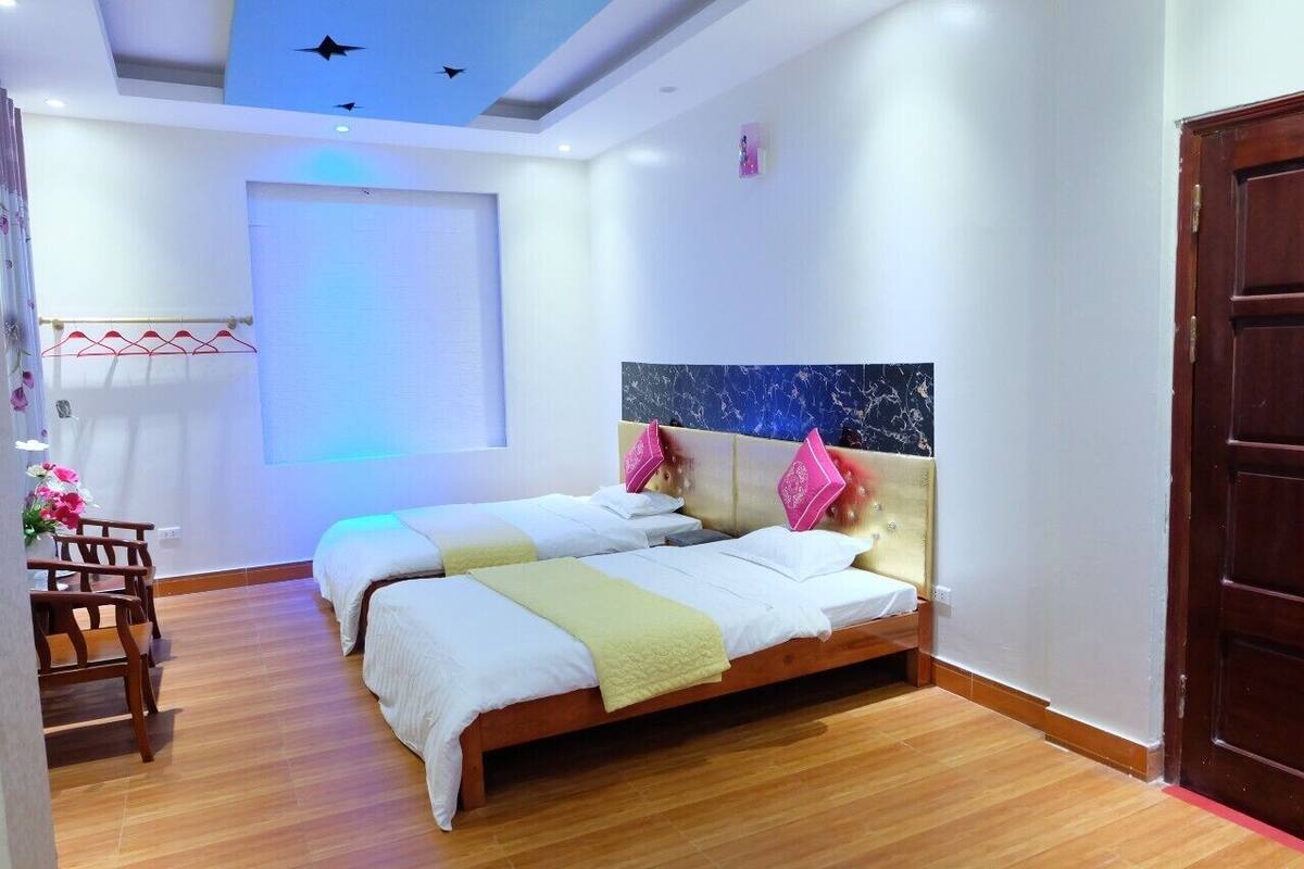 A hotel room with two beds, a wooden floor, a ceiling with star decorations, and a large window.