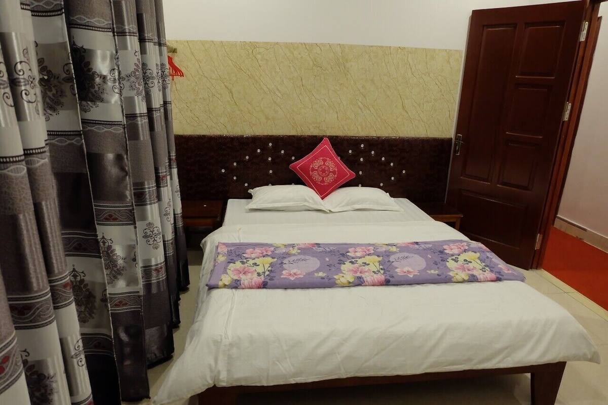 A neatly made bed with white linens and a floral pillow, a purple blanket, and a headboard with a decorative red pillow.