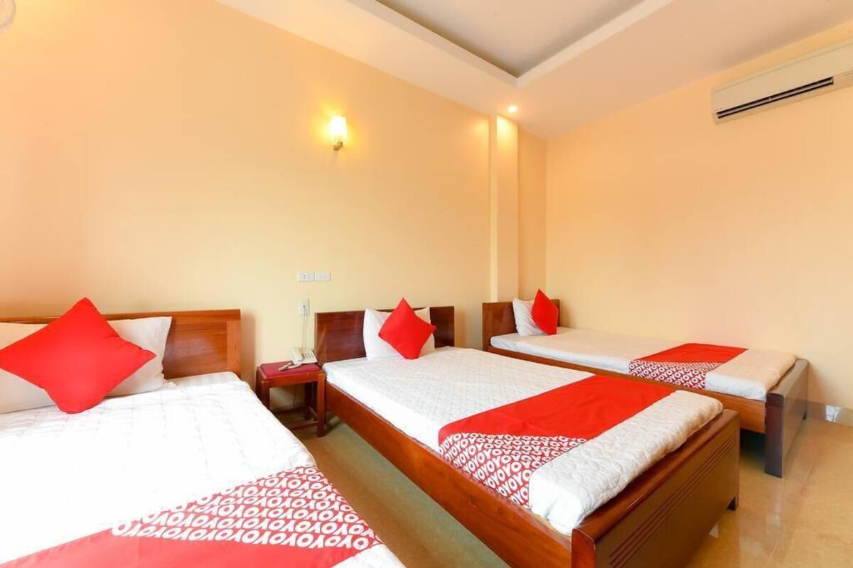 A hotel room with three single beds, each with a red and white patterned bedspread and matching pillows.