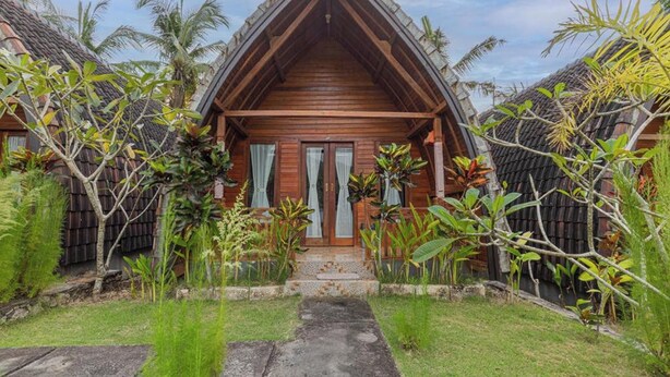 Uma casa de madeira com telhado triangular, rodeada por vegetação exuberante e palmeiras.