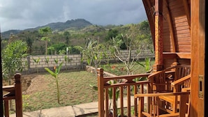 Um deck de madeira com vista para um jardim ajardinado e colinas ao longe.