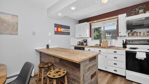 Una cocina moderna con armarios blancos, una isla de madera y un ventanal grande.