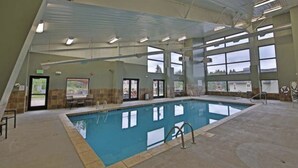 Una piscina interior con paredes de vidrio transparente, suelo de baldosas e iluminación fluorescente en el techo.