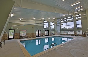 An indoor swimming pool with clear glass walls, a tiled floor, and a ceiling with fluorescent lighting.