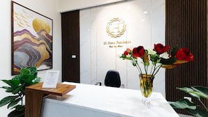 Un comptoir d’accueil avec un mur en marbre, une œuvre d’art encadrée, un logo et un vase rempli de fleurs.