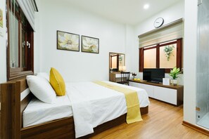 Una habitación de hotel con una cama de madera, un escritorio con televisor, un espejo y dos cuadros de flores en la pared.