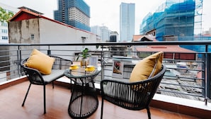 Un balcon avec deux fauteuils en osier, une petite table et des coussins jaunes.