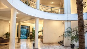 Un interior espacioso con una escalera curva, pilares grandes y plantas en macetas.