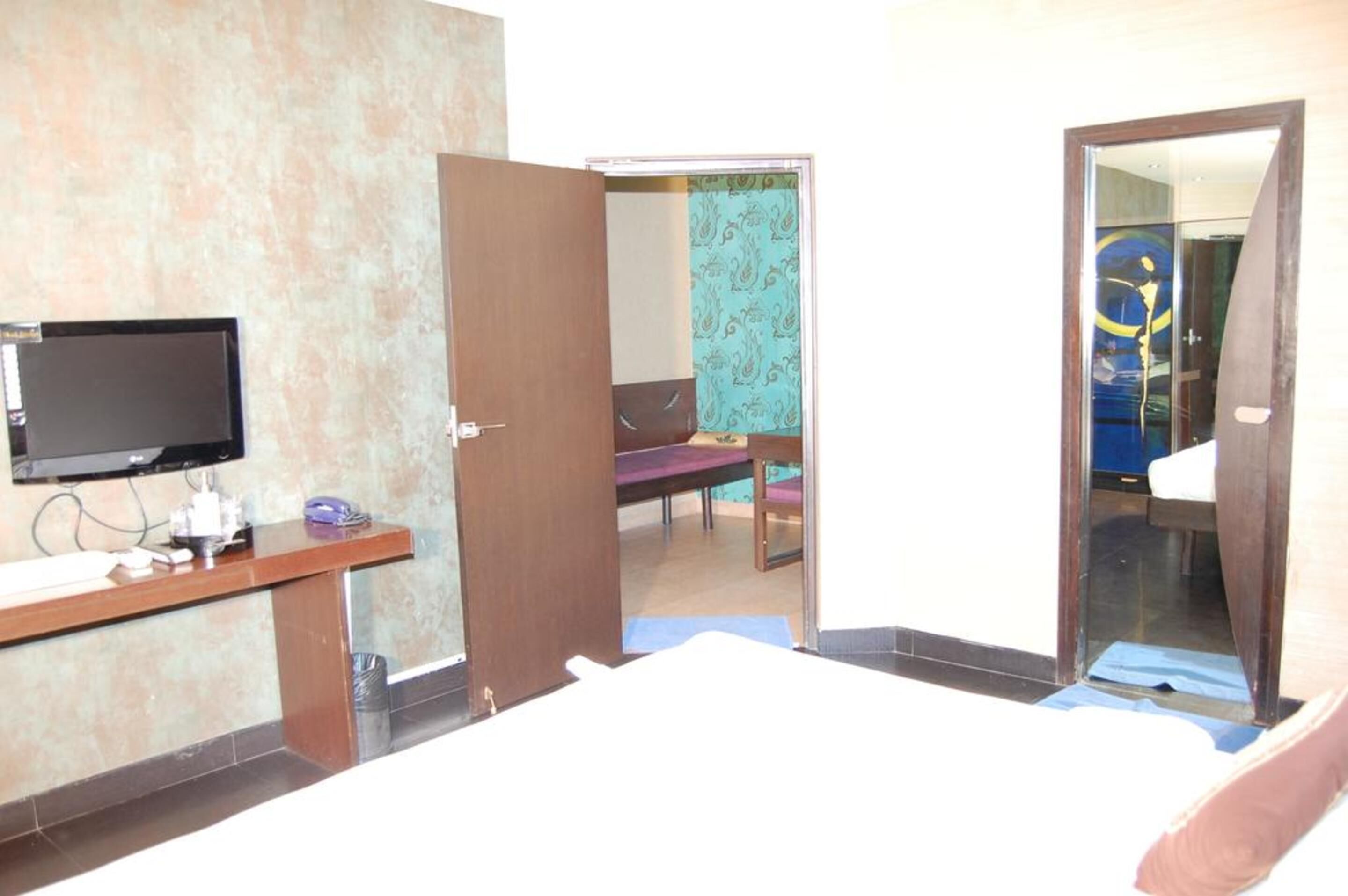 Una camera d'albergo con un letto, una scrivania con televisione a schermo piatto, un telefono e uno specchio.
