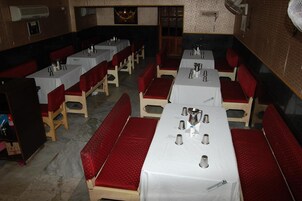 Um restaurante com várias mesas e cabines, cada uma com toalhas brancas e assentos estofados vermelhos.