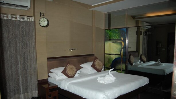 A hotel room with a large bed, a clock on the wall, and a mirror reflecting the room.