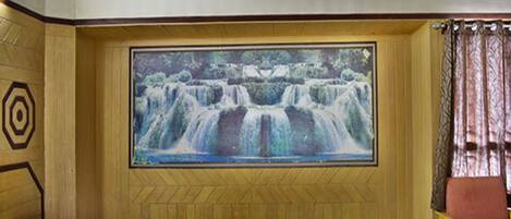 A room with a bed, a chair, and a large painting of a waterfall on the wall.