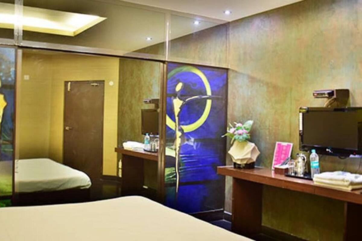 A hotel room with a bed, a desk with a computer, a mirror, and a wall with a painting.