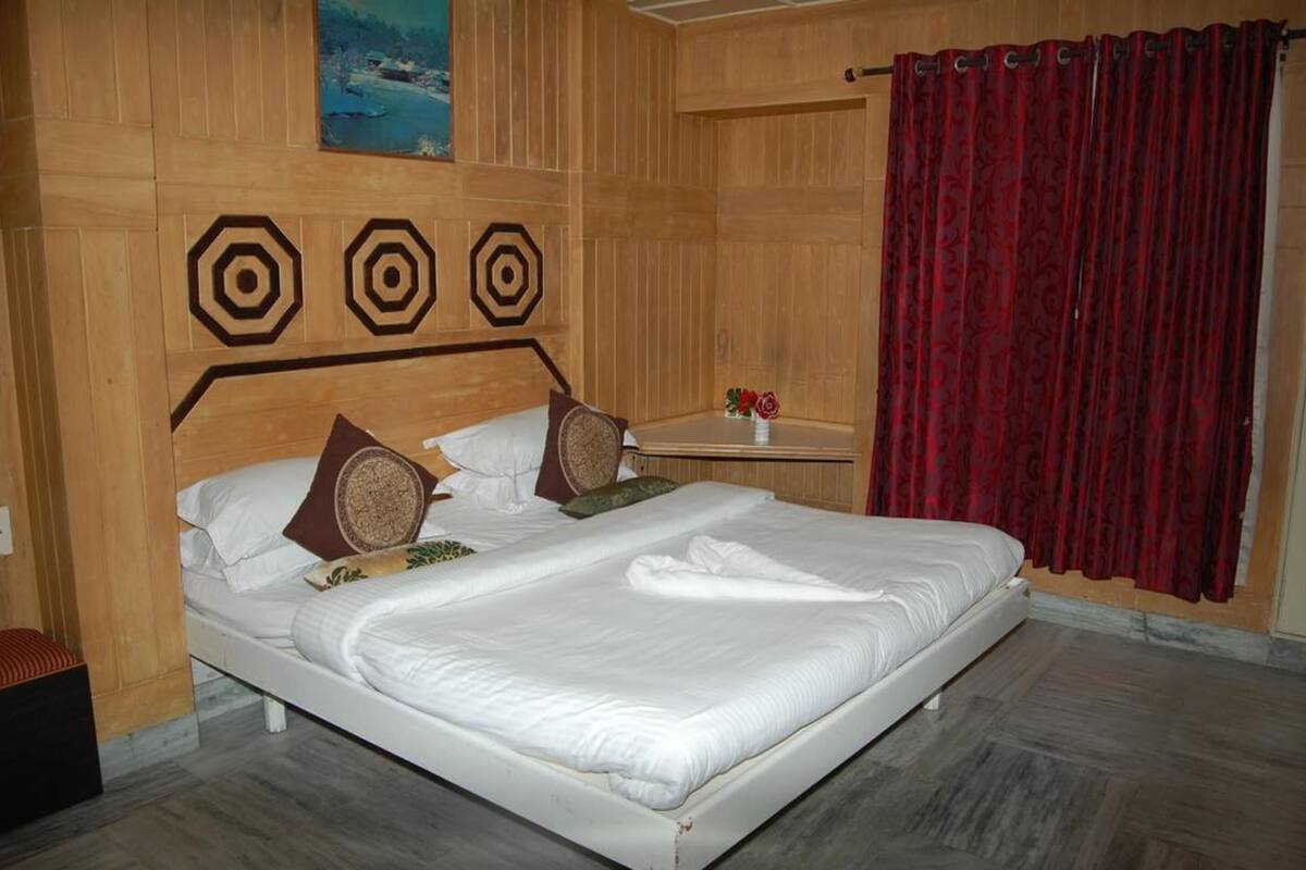 A neatly made bed with white linens, a wooden headboard with geometric patterns, and a red curtain on the window.