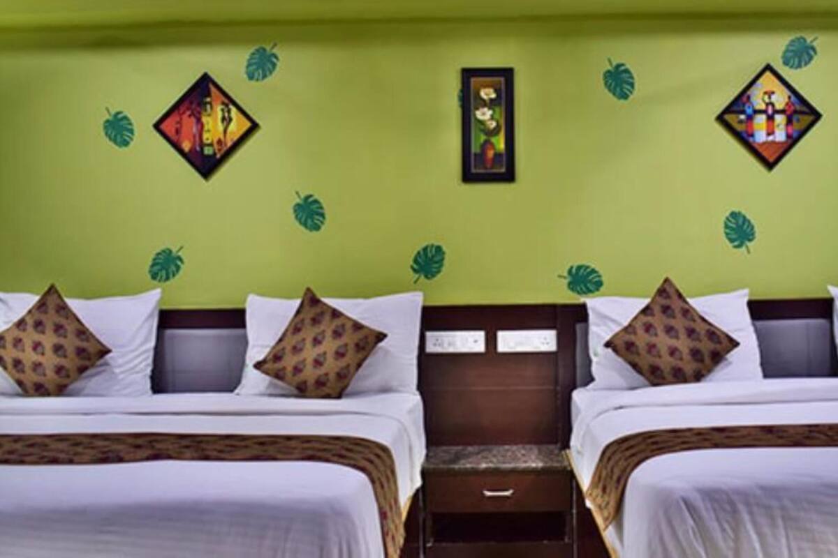 A hotel room with two beds, each with white bedding and patterned pillows. There are wall decorations including a framed picture and a small painting.
