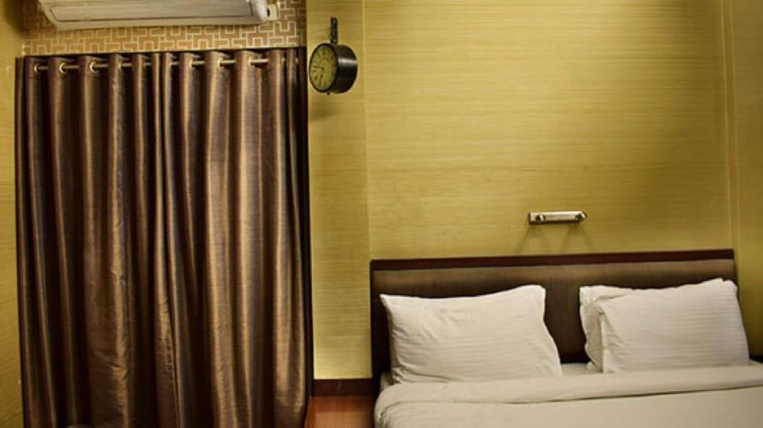 Een hotelkamer met een bed, gordijnen, een klok en een thermostaat.