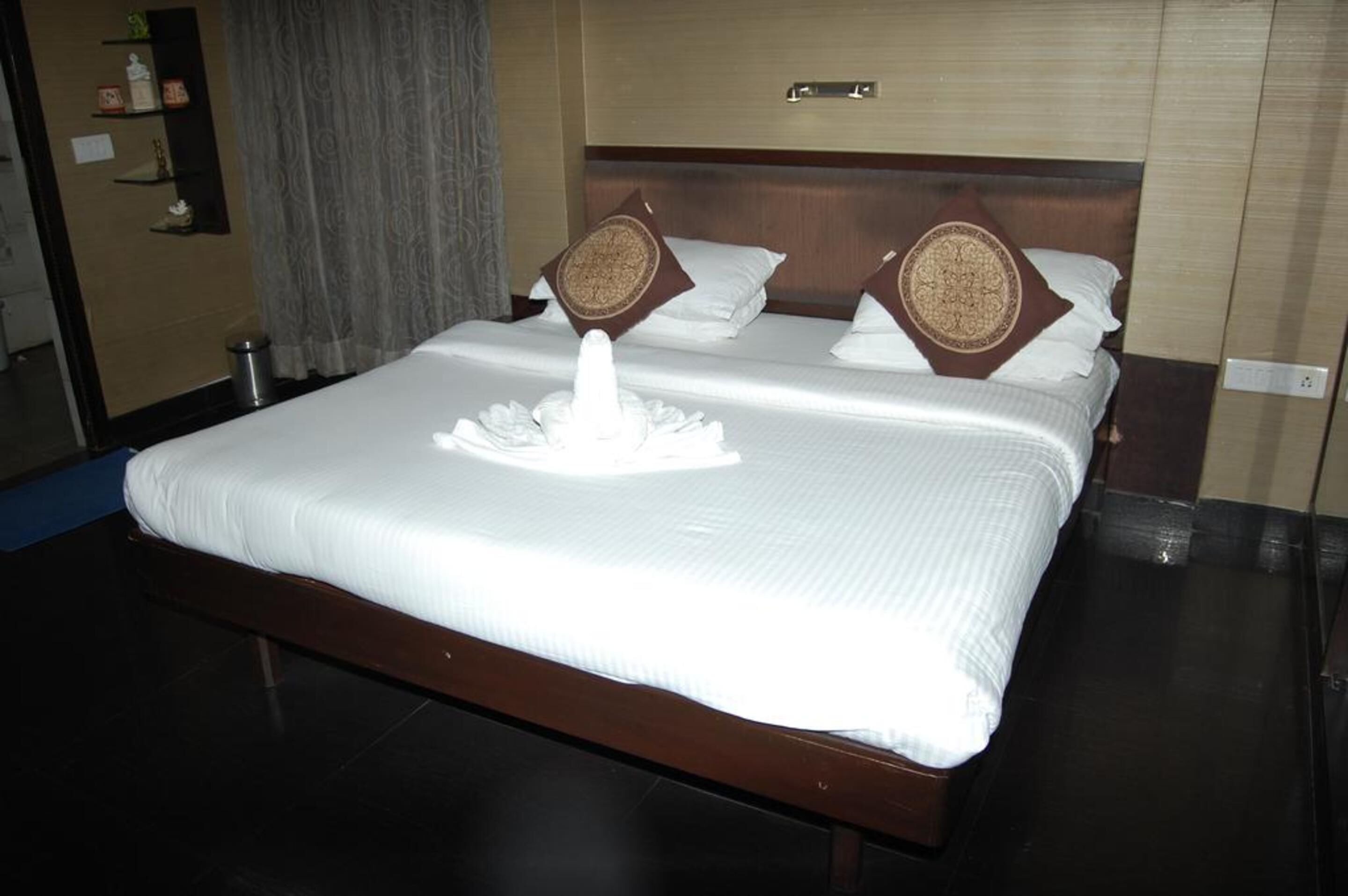 A hotel room with a large bed, two pillows, a bedside table, and a wall-mounted shelf.