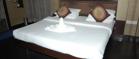 A hotel room with a large bed, two pillows, a bedside table, and a wall-mounted shelf.