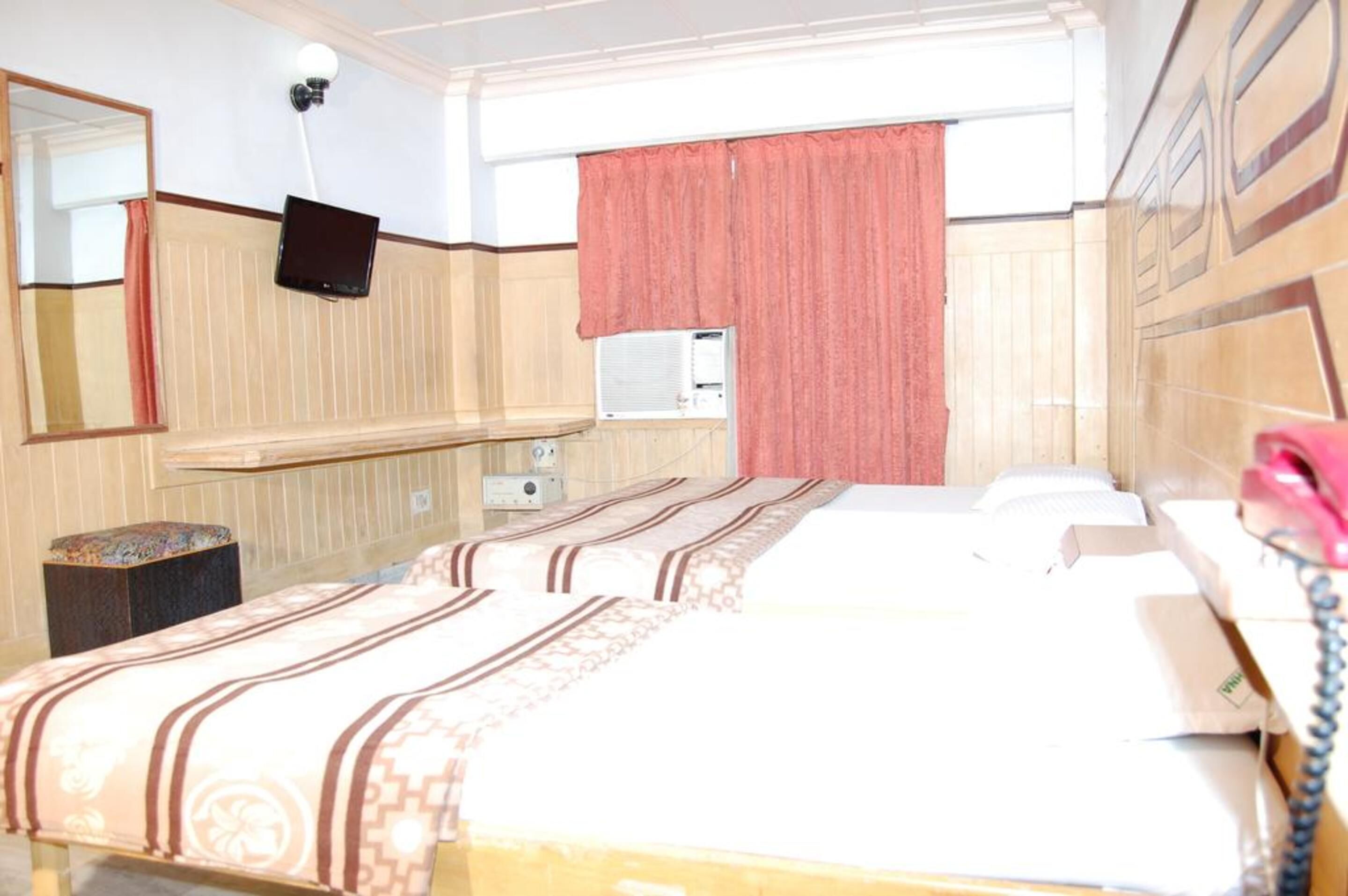 Ein Hotelzimmer mit zwei Betten, einem Spiegel, einem Fernseher, einer Klimaanlage und einem Telefon.