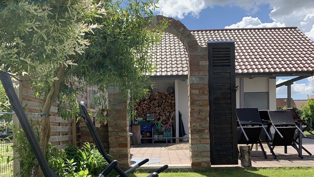 A patio area with outdoor furniture, a brick wall, and a view of a building with a tiled roof. - House with winter garden and patio (Burgheim)