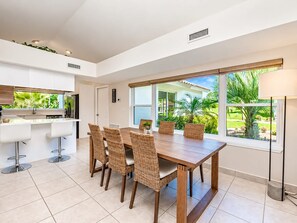 A modern kitchen with white cabinets, a dining table with wicker chairs, and a large window with a view of greenery. - SWISS 66 - Lake Denise (Clermont)