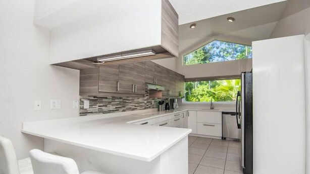 Une cuisine moderne avec des meubles blancs, un îlot central et une grande fenêtre donnant sur un paysage verdoyant.