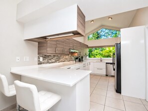 A modern kitchen with a large island, white cabinetry, and a view of greenery outside. - SWISS 66 - Lake Denise (Clermont)