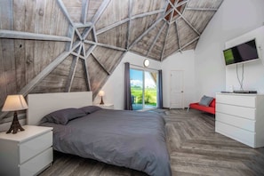 A bedroom with a sloped ceiling, a bed, a nightstand, a dresser, a TV, and a sliding glass door leading to an outdoor area. - STUDIO 01 - Lake Sumner (Clermont)