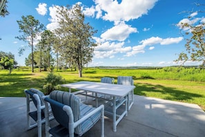 An outdoor patio with a table and chairs, surrounded by trees and a grassy field. - STUDIO 01 - Lake Sumner (Clermont)