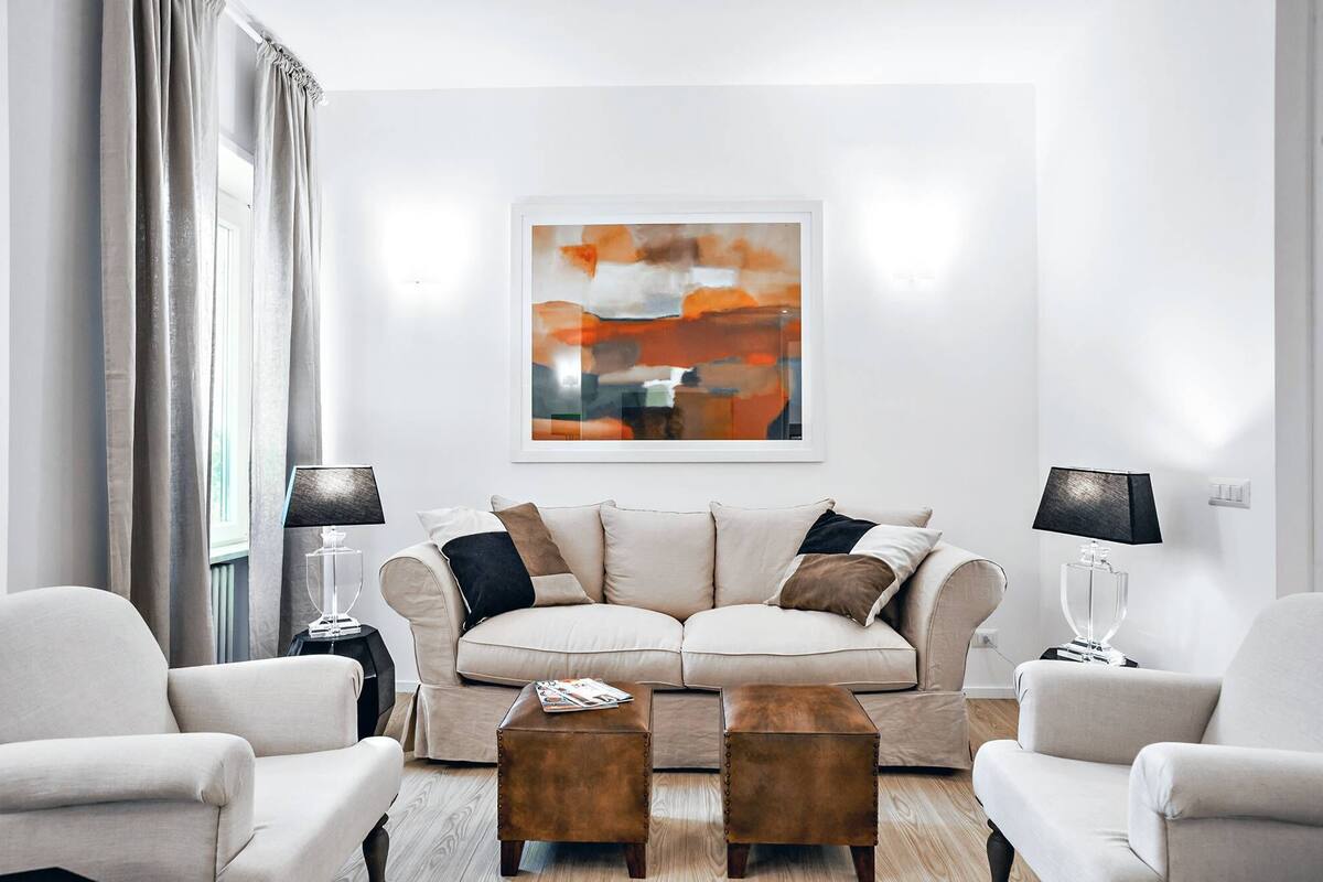 A modern living room with a beige sofa, two armchairs, a coffee table, and a framed abstract painting.