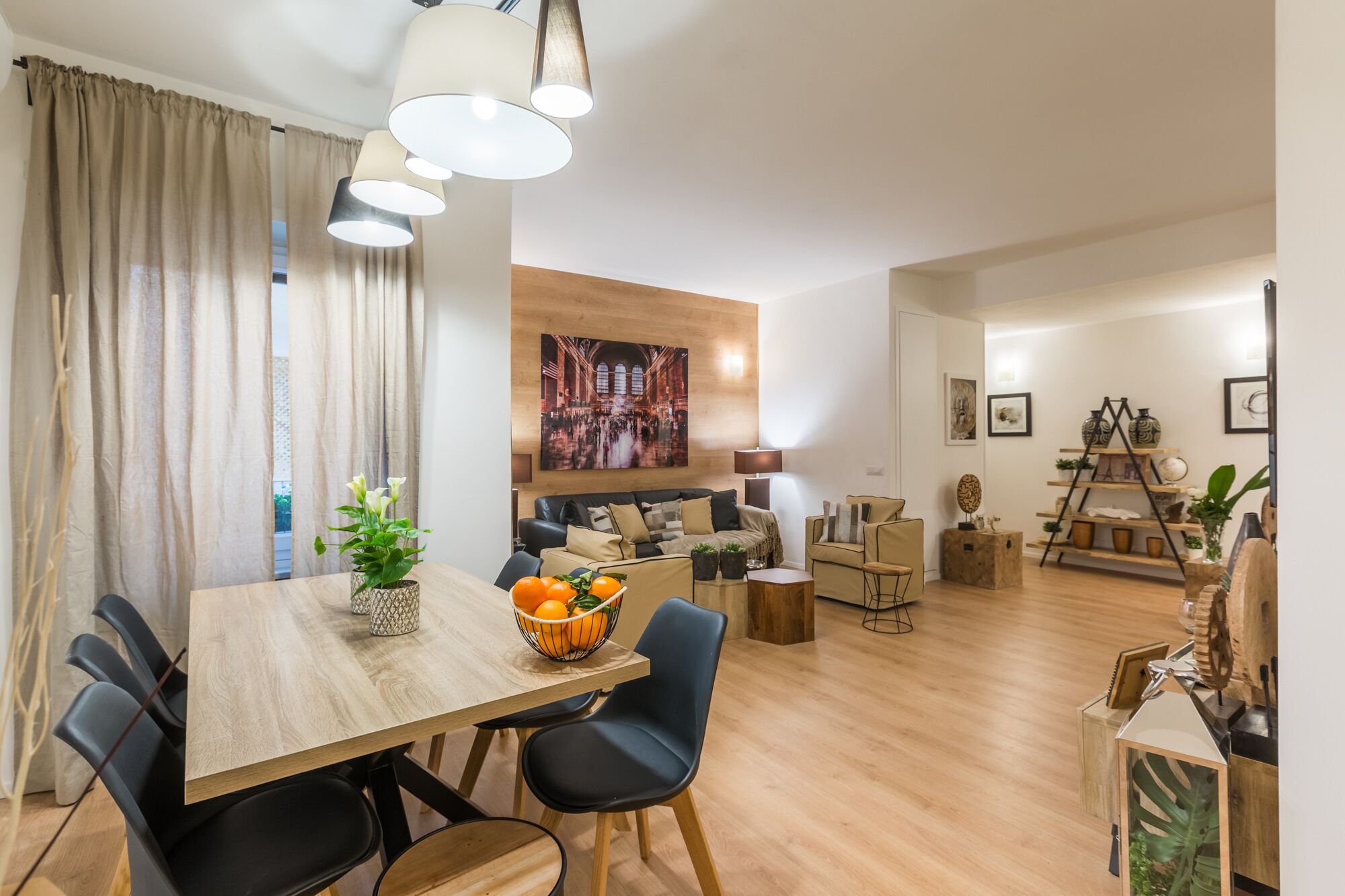 Un salon moderne avec une table à manger en bois, des chaises noires et un canapé. Un tableau est accroché au mur et une plante est posée sur la table.