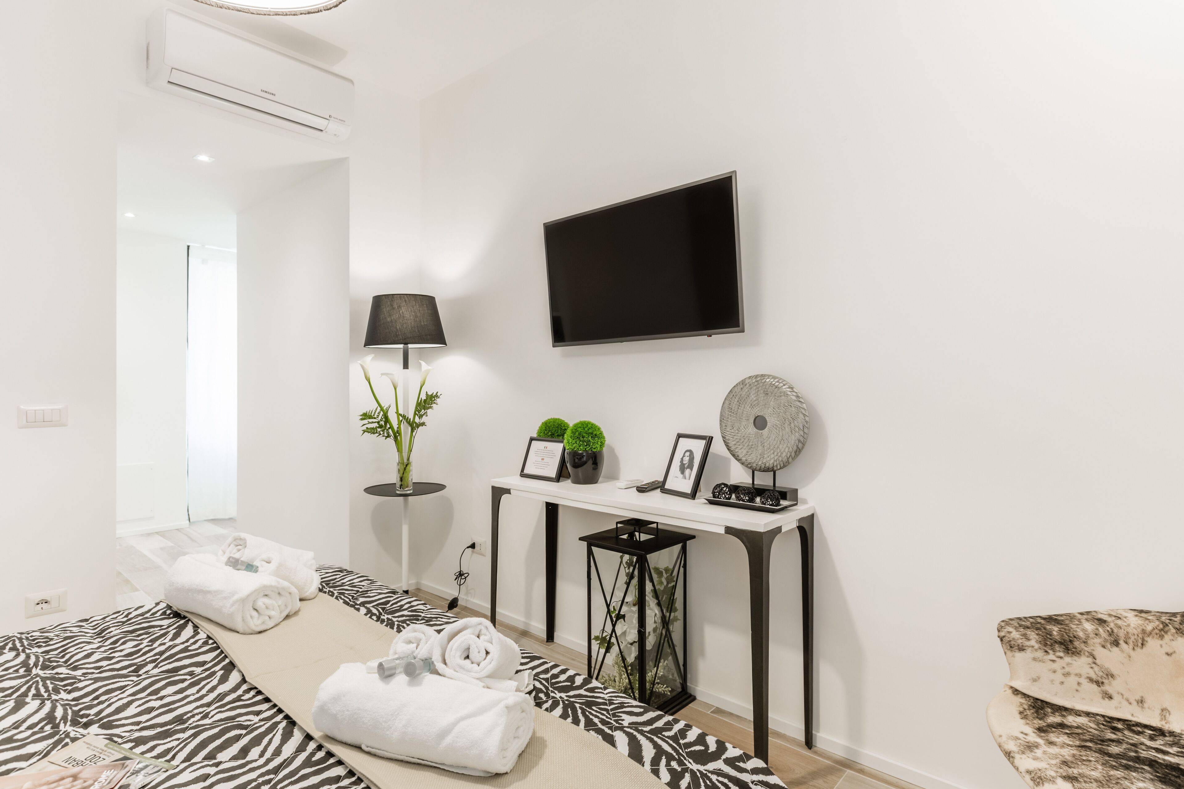 A modern hotel room with a bed, a flat-screen TV, a desk with a lamp, and a chair.