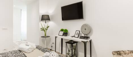 A modern hotel room with a bed, a flat-screen TV, a desk with a lamp, and a chair.