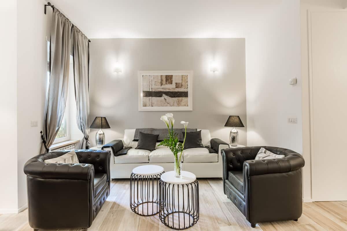 A modern living room with a sofa set, two side tables, and a decorative vase with flowers.
