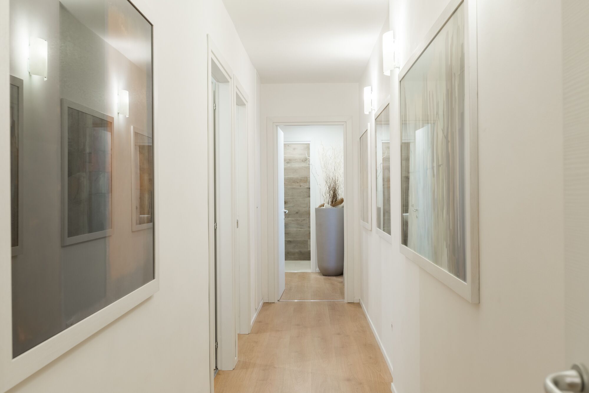 Un pasillo estrecho con paredes blancas, suelo de madera y puertas que dan a varias habitaciones.