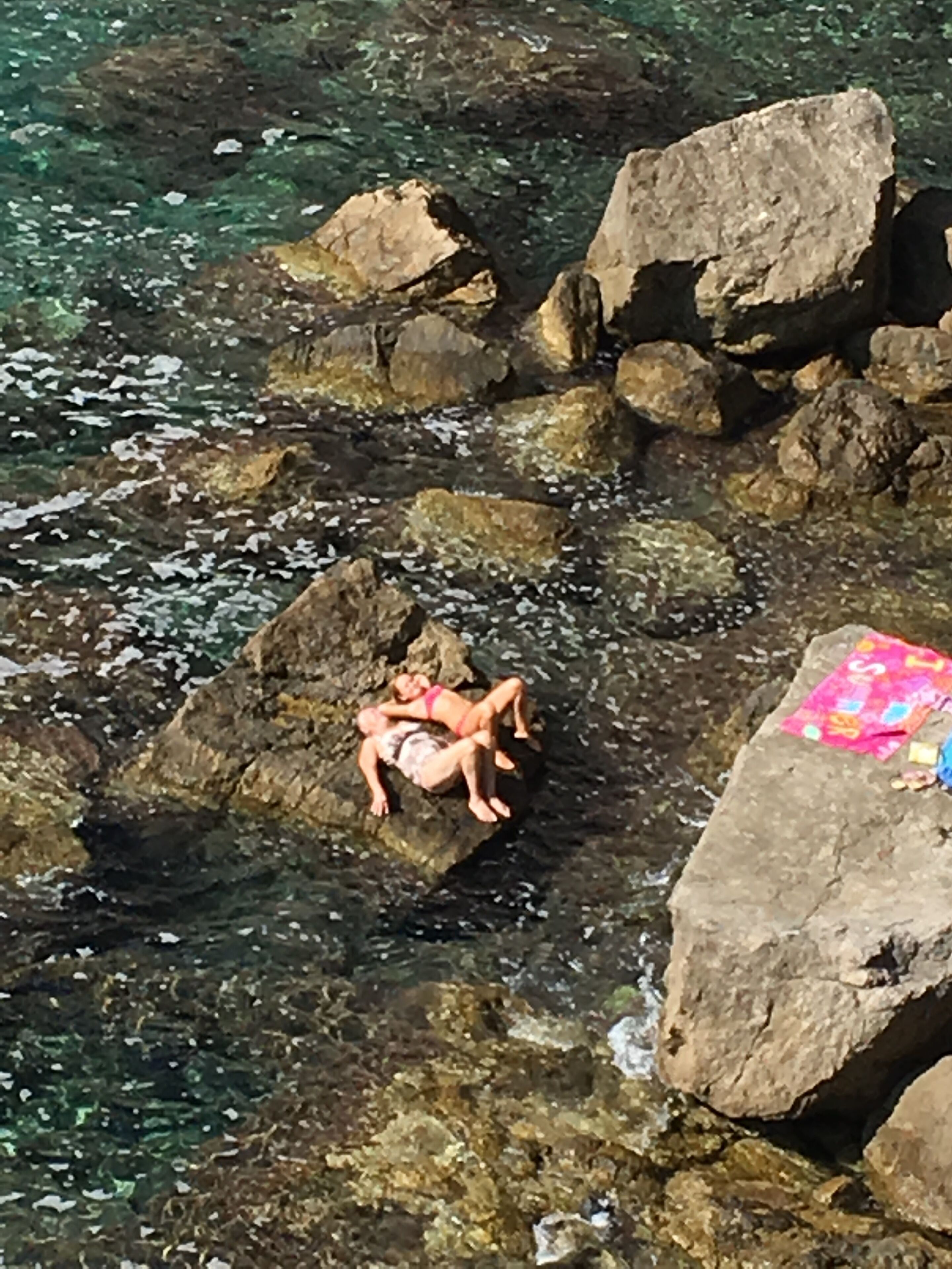 A person lying on rocks by a clear body of water.