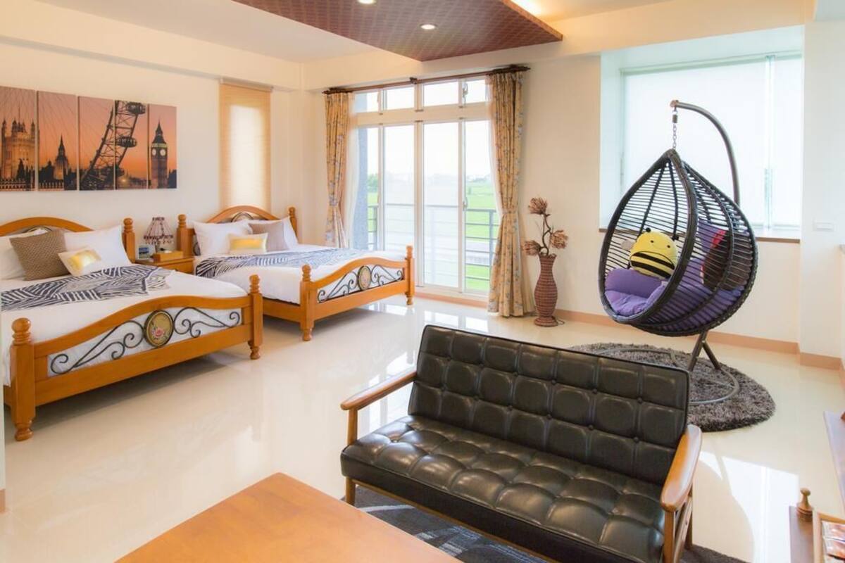 A hotel room with two wooden beds, a black leather sofa, and a hanging chair.