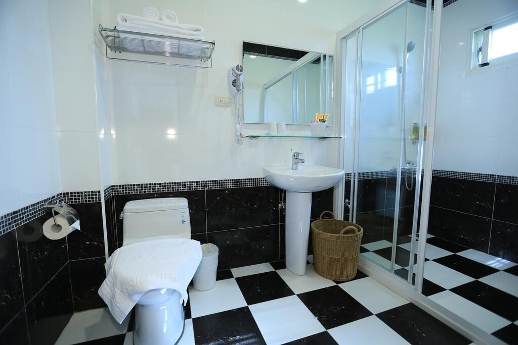 A bathroom with a black and white checkered floor, a white sink, a glass shower enclosure, and a white toilet.